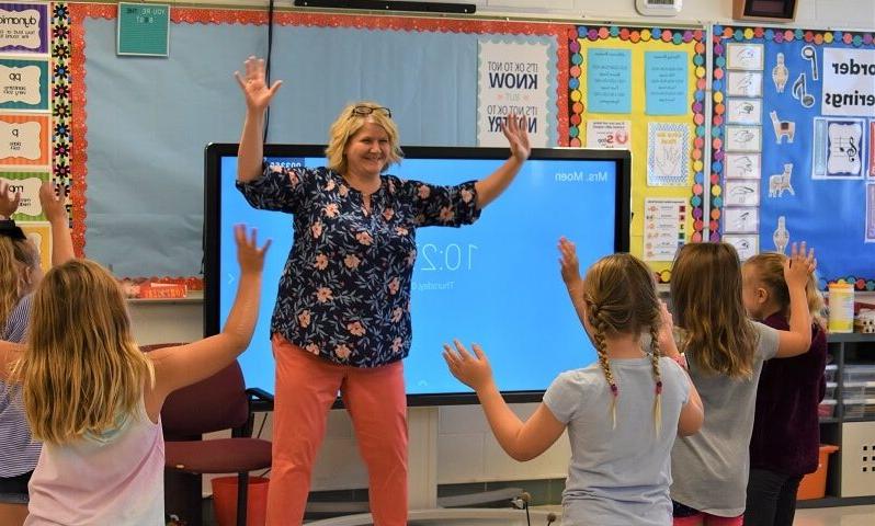 music teacher and young children holding their arms up while moving to the beat of a song